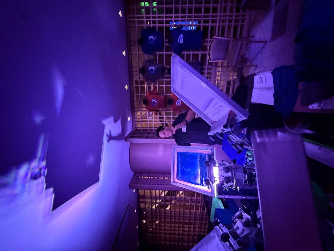 Print station and garment display wall glowing under purple event lighting